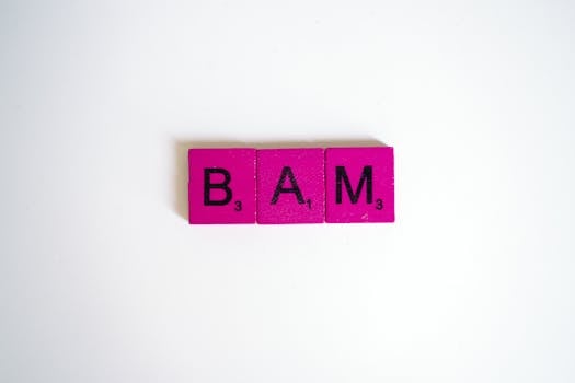 Close-up of pink Scrabble tiles spelling 'BAM' on a white background, conveying expression.