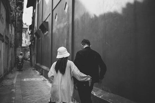Man in Black and Woman in White Striped Long Sleeve Shirt and Black Pants Walking on Sidewalk