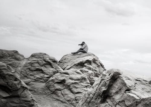 Man Taking Photos Sitting on Rocky Mountains