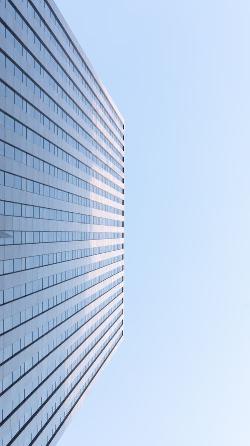 Free Modern skyscraper with glass facade reaching into a cloudless blue sky. Stock Photo