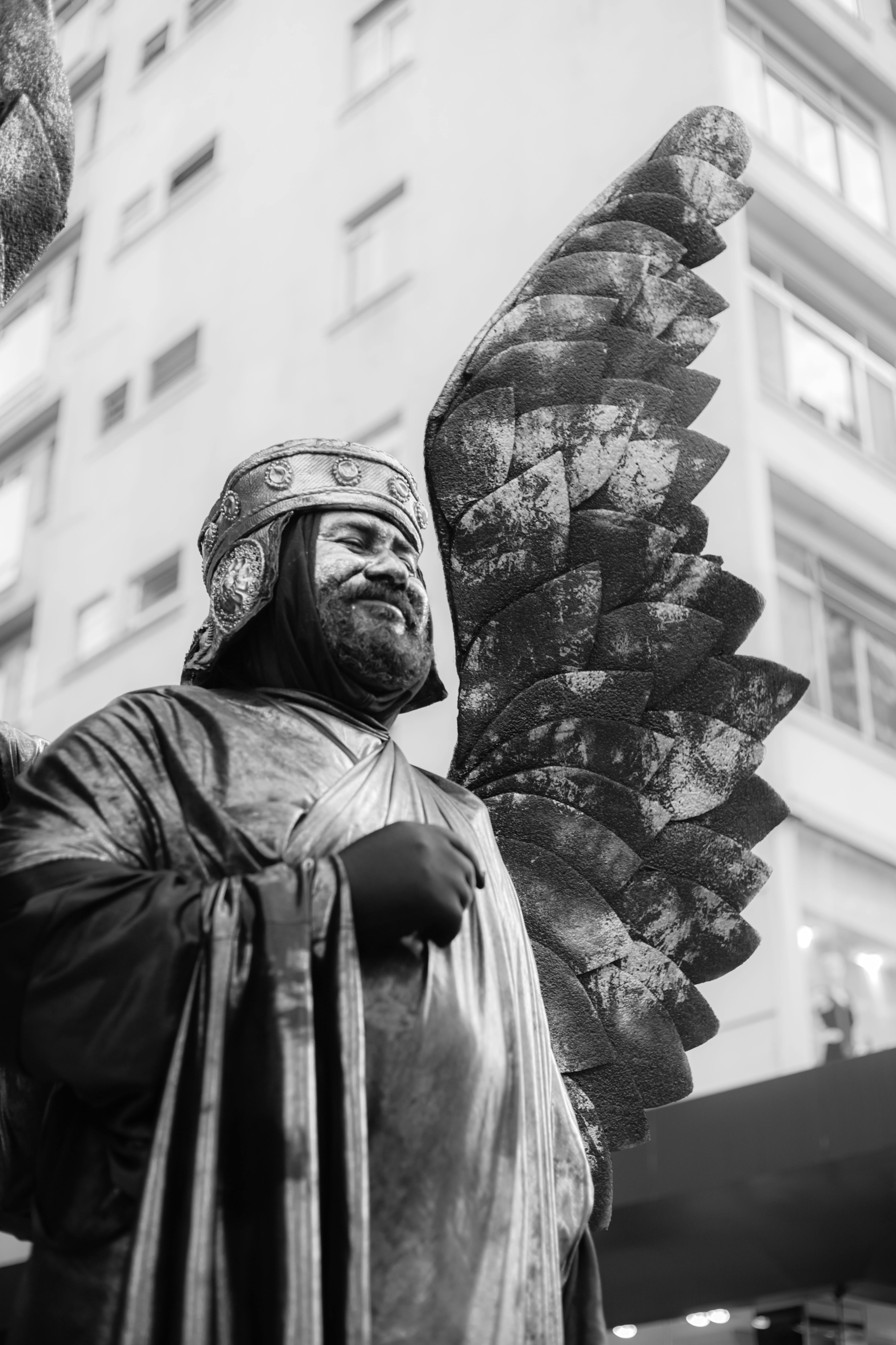 grayscale photo of man in black jacket standing near statue