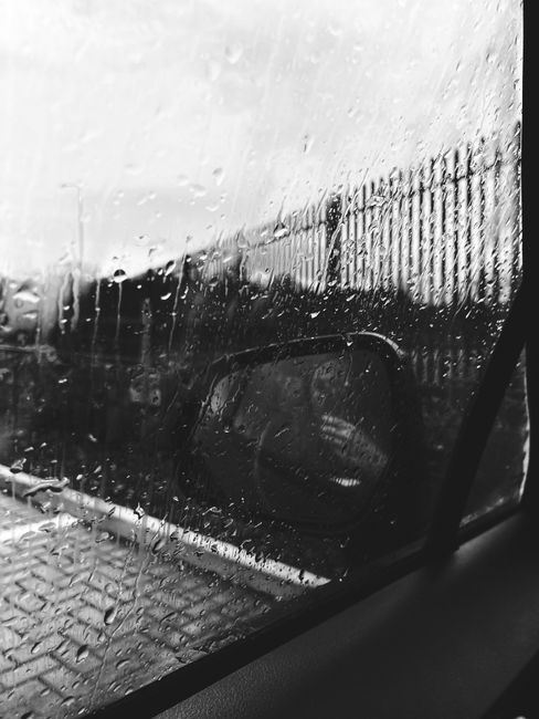 Black and white faceless driver taking photo of car window and rear viewer covered with raindrops