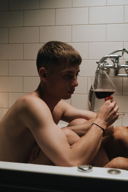 Free A man indulges in a glass of wine while sitting in a white-tiled bathroom. Stock Photo