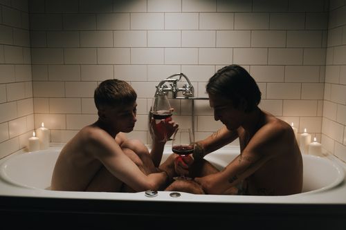 Free A tender scene of a couple enjoying wine in a bathtub, surrounded by candlelight. Stock Photo
