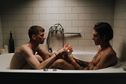 Free Two tattooed men share an intimate moment in a bathtub, surrounded by a cozy ambiance with candles. Stock Photo
