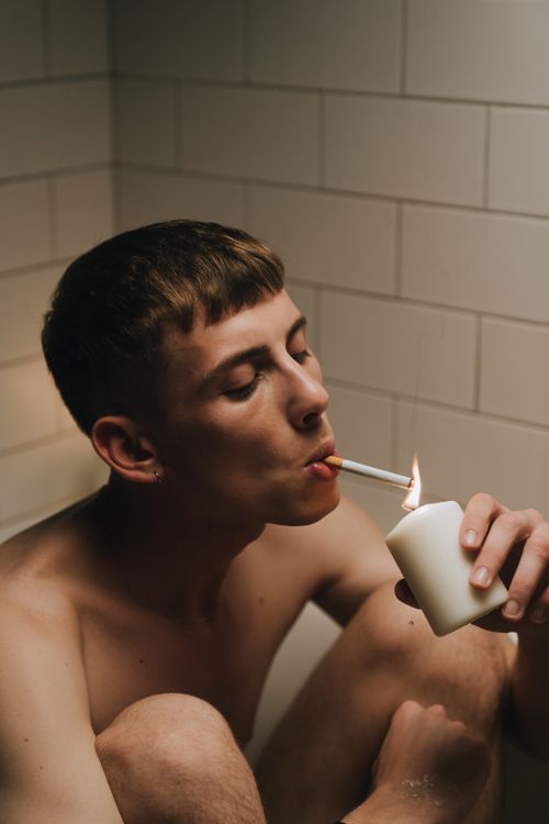 Free Male lighting a cigarette with a candle while seated in a bathroom setting. Stock Photo