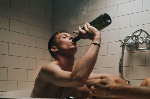 Free A young man in a bathtub smoking and drinking wine, relaxed and carefree. Stock Photo