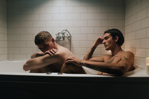 Free Two tattooed men share a reflective moment in a bathtub, highlighting intimacy and connection. Stock Photo