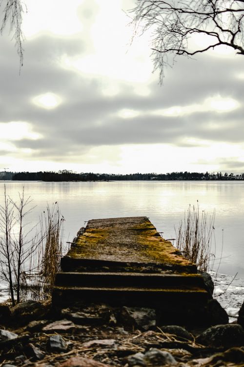 Free Weathered wooden pier extends into tranquil lake under a cloudy sky in Helsinki, Finland. Stock Photo