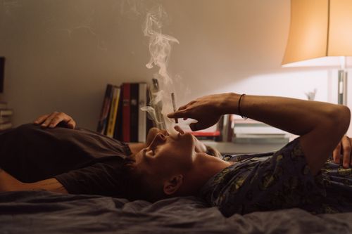 Free Two adults relaxing indoors, one smoking under soft lamp light with a serene atmosphere. Stock Photo