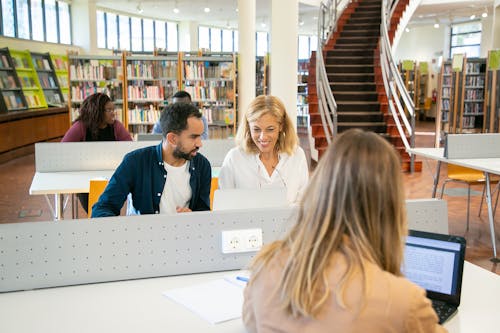 Free Young students preparing for exams using laptops in library Stock Photo
