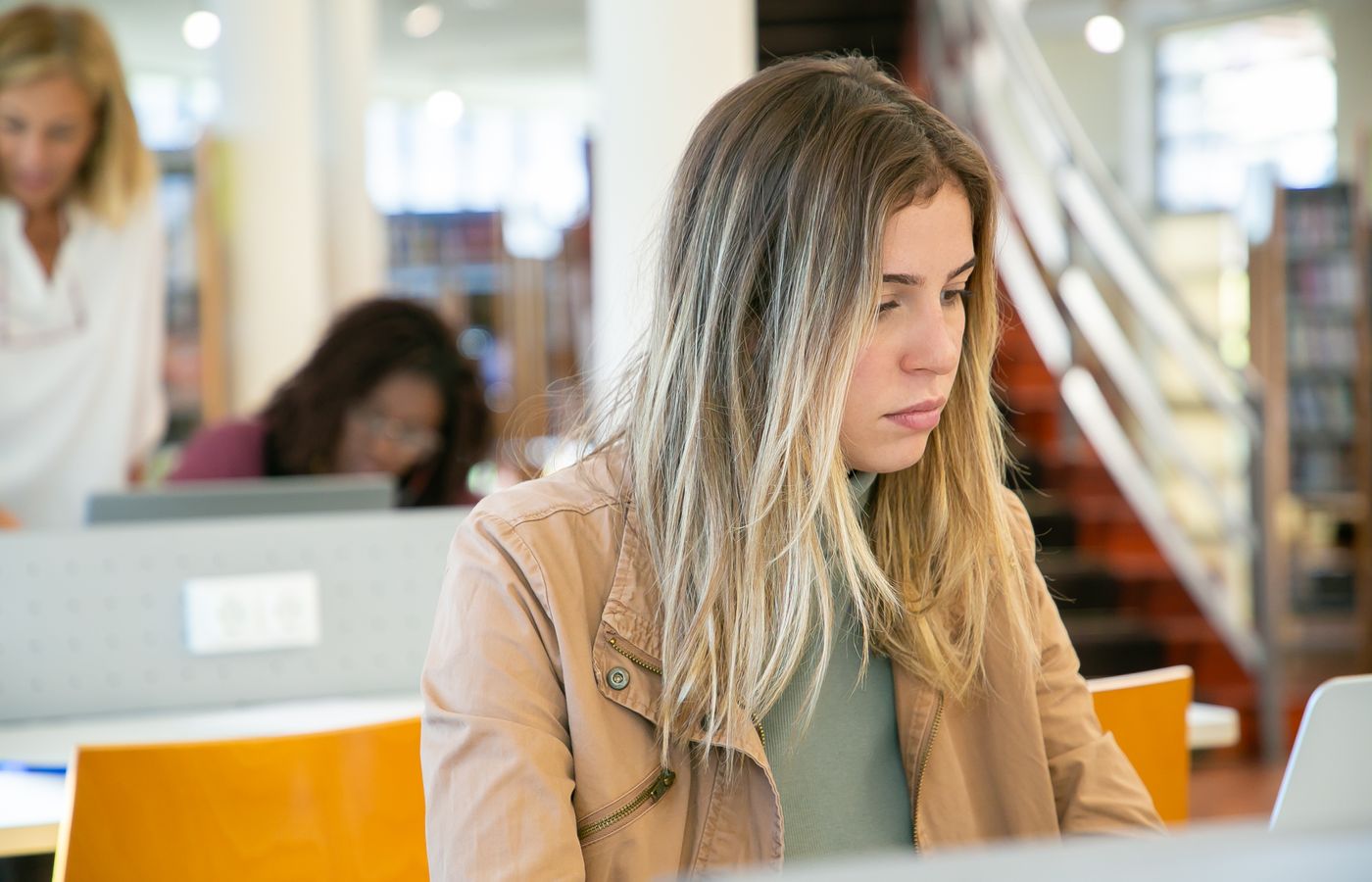 Young woman studying on laptop in a university library, focusing deeply on her work.
