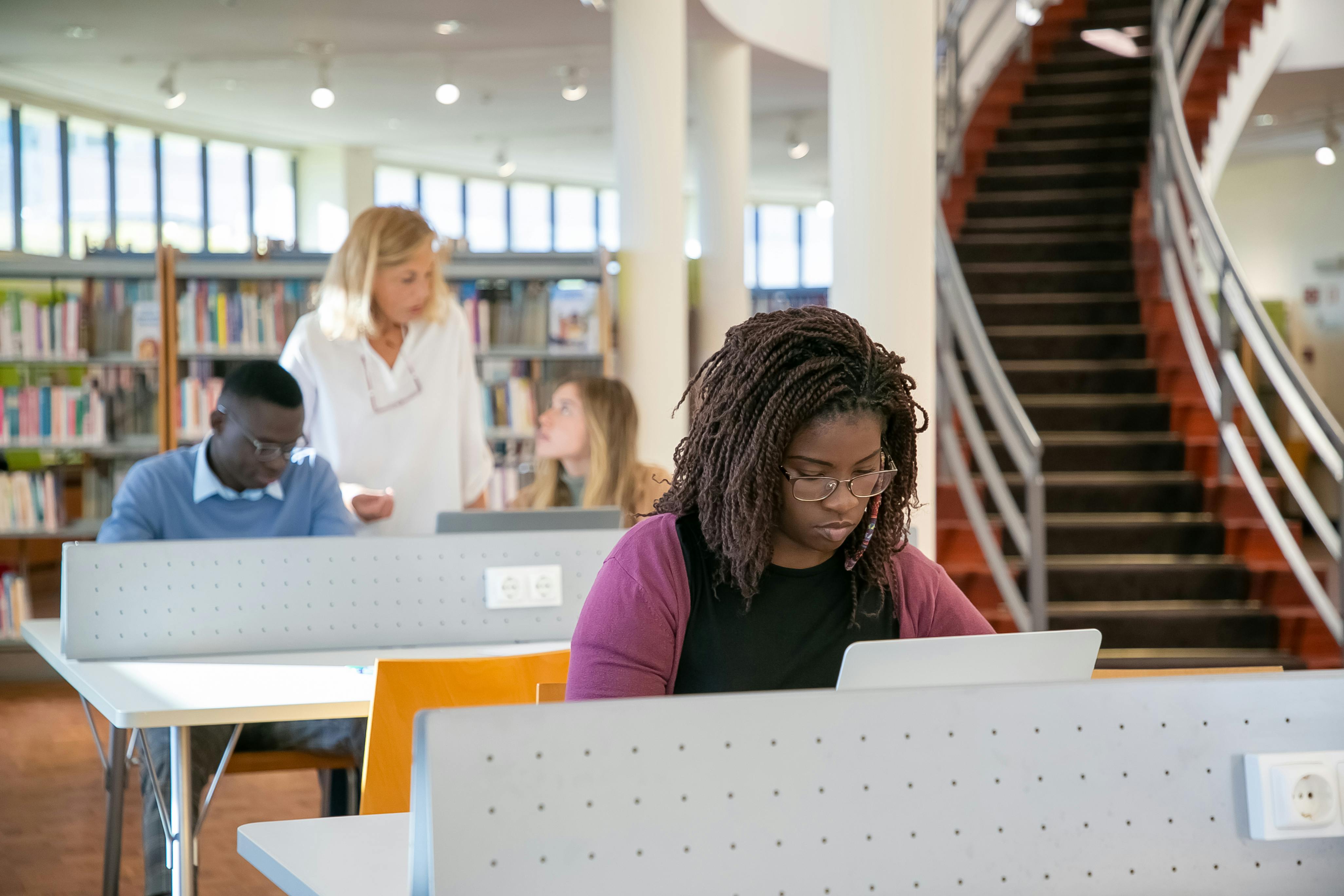 concentrated young diverse students using laptops during lesson in library