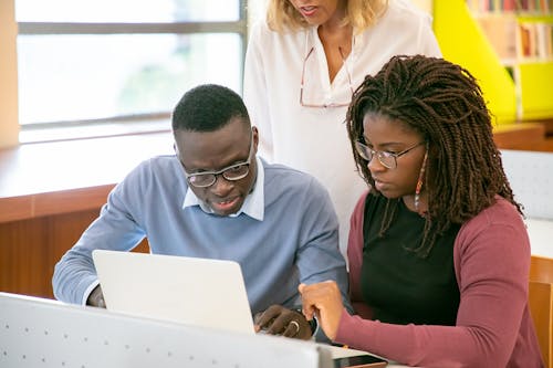 Attentive young black groupmates using laptop while preparing for exams with anonymous teacher