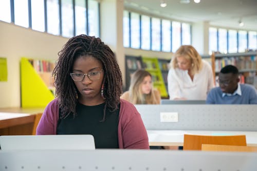 Focused multiracial students doing presentation in library with teacher