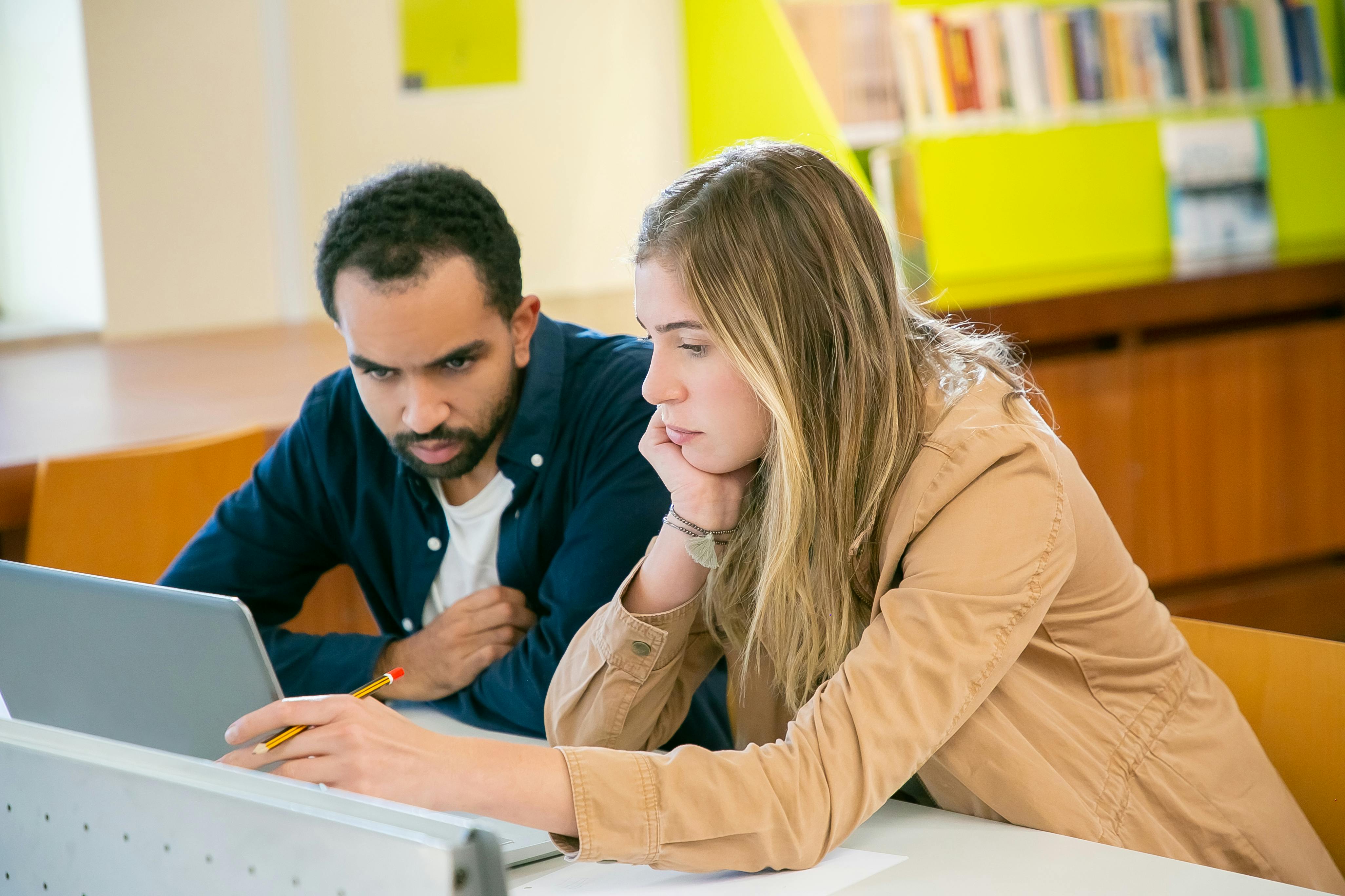 Free Concentrated multiracial classmates using laptop for studies while doing homework assignment together in university Stock Photo