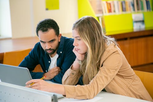 Concentrated multiracial classmates using laptop for studies while doing homework assignment together in university