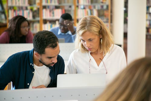 Serious ethnic bearded male student preparing study task and explaining project details to teacher in university library