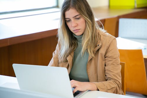Free Crop concentrated female freelancer sitting at table and browsing laptop while working online on project Stock Photo