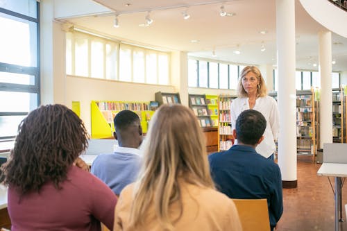 Group of multiracial classmates having seminar with teacher in university library during studies