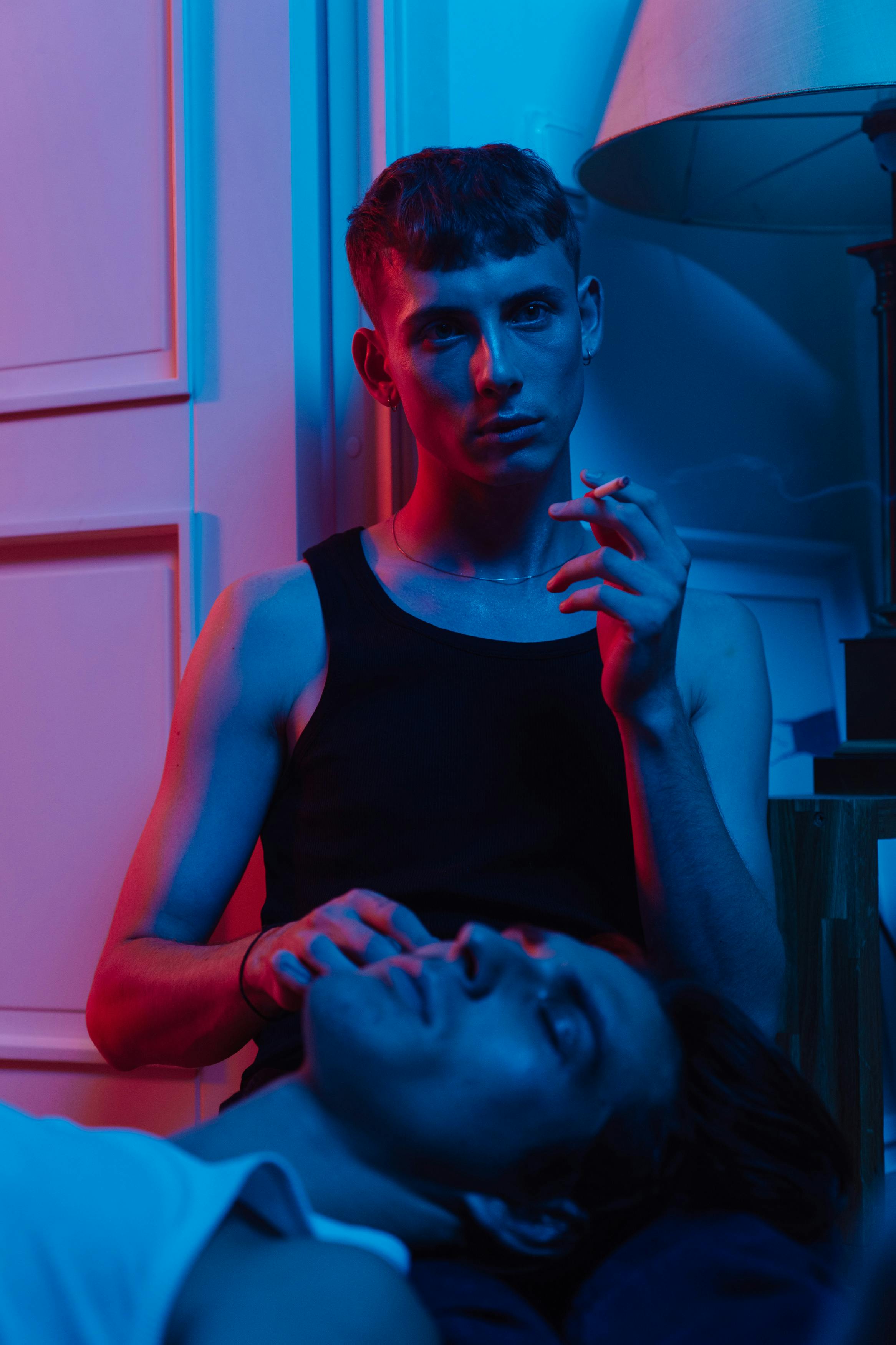 Two young adults in artistic lighting, one smoking a cigarette, creating a dramatic and moody scene.