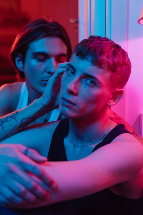 Free Close-up portrait of two young men embracing in vibrant neon lighting, expressing love and togetherness. Stock Photo