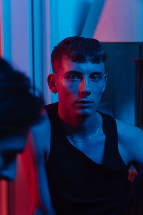 Free Portrait of a young man in dramatic red and blue neon lighting, creating a moody atmosphere. Stock Photo