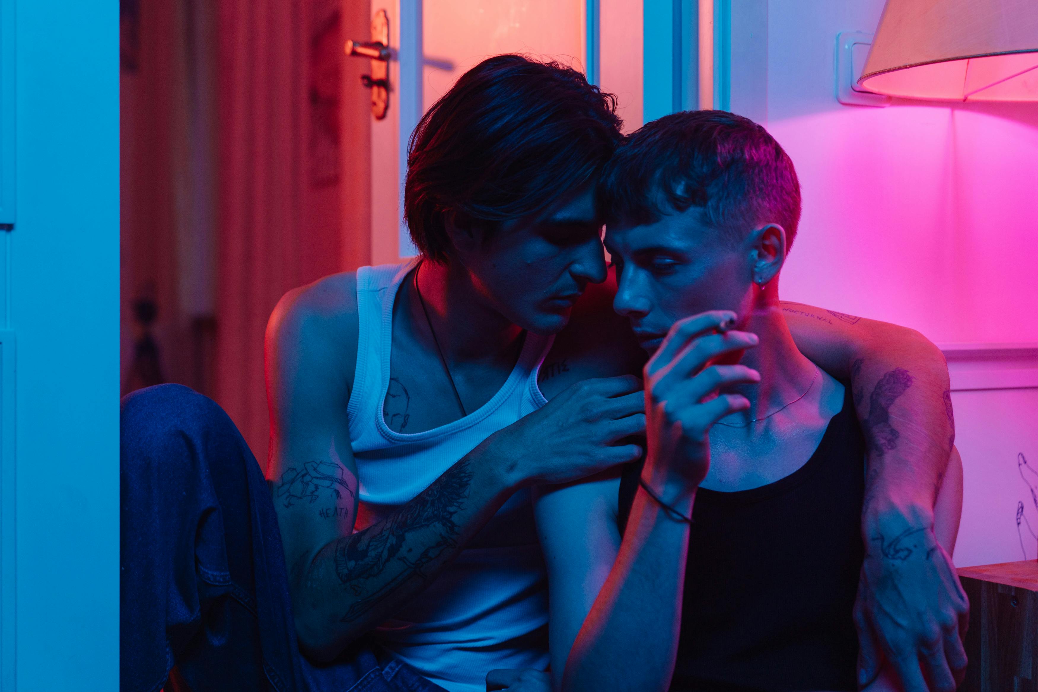 Close-up shot of a loving LGBT couple embracing under moody neon lighting indoors.