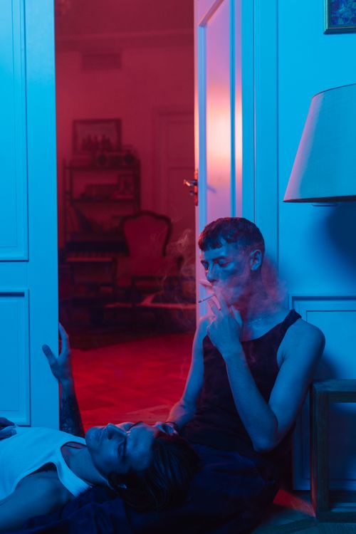 Free Two young adults in a dimly lit room, one smoking, creating a moody and atmospheric vibe. Stock Photo