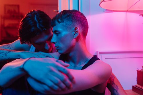 Free A tender embrace between two men under colorful lighting, capturing love and intimacy. Stock Photo