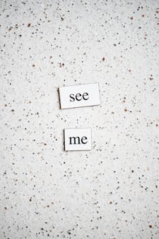 Typography art featuring the words 'see me' on a speckled surface, conveying a simple yet intriguing message.