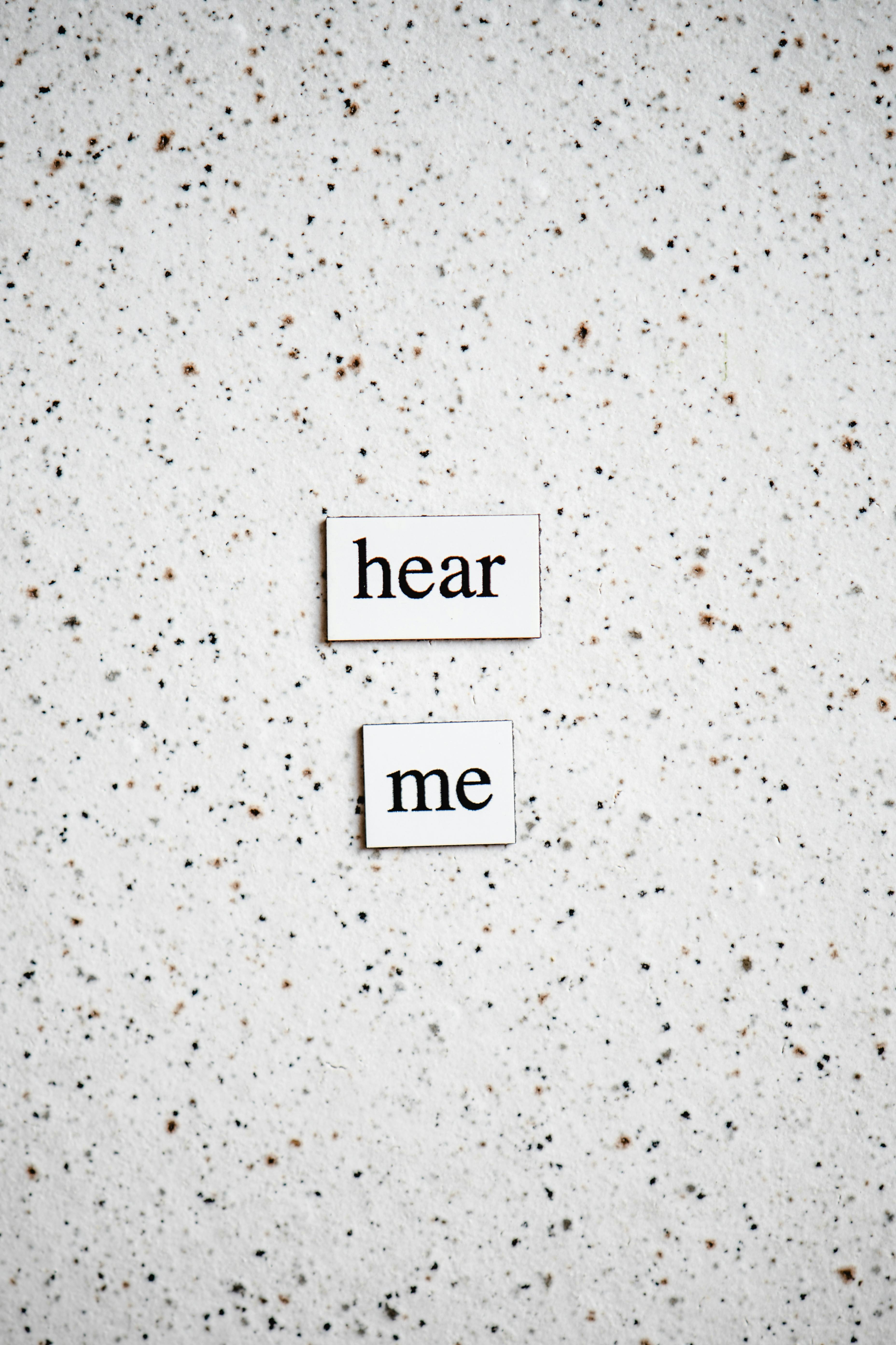 Minimalist photo of 'hear me' text tiles on a speckled surface, perfect for communication themes.