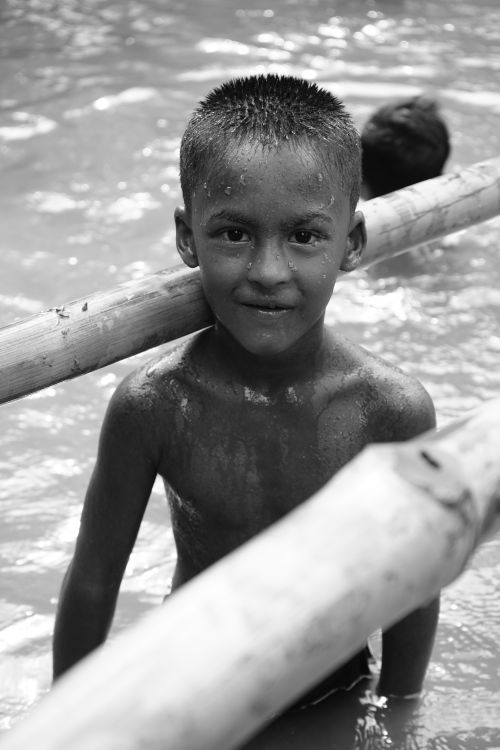 Free A joyful South Asian boy playing in water with bamboo poles in Manikganj, Bangladesh. Stock Photo