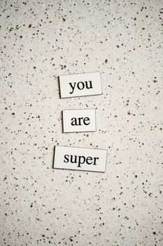 Vertical image of 'You are super' text tiles on a speckled surface.