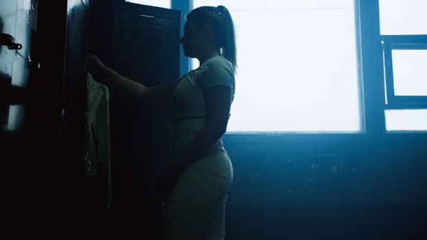 Silhouetted woman organizing clothes in a locker room.