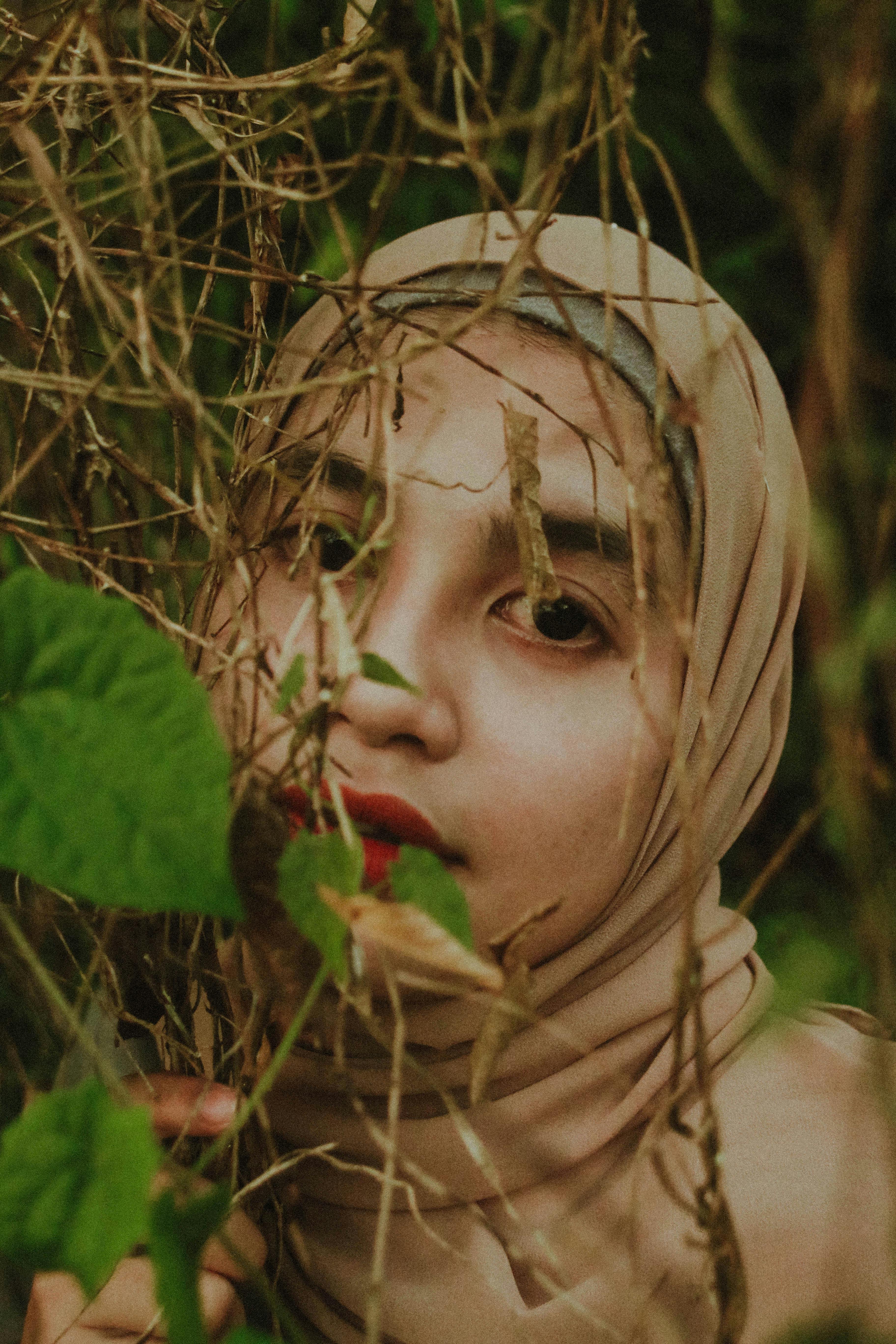 A woman wearing a hijab surrounded by foliage, exuding a natural and serene vibe.