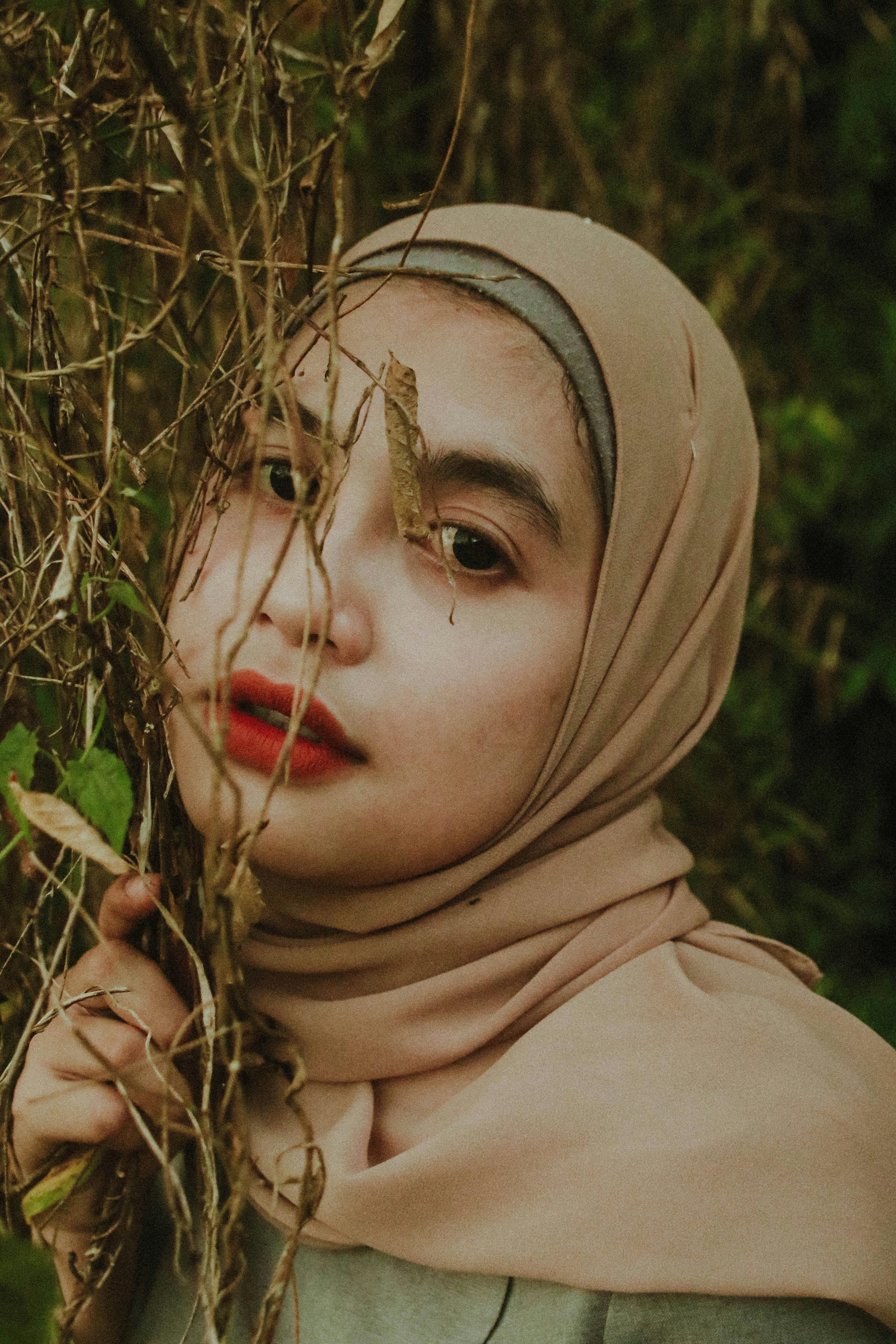 Close-up portrait of a woman in a hijab surrounded by nature, evoking serene and earthy vibes.