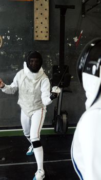 Two fencers in full gear engage in a lively indoor fencing match.