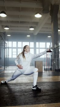 Young woman fencer performing a lunge in an indoor gym setting.