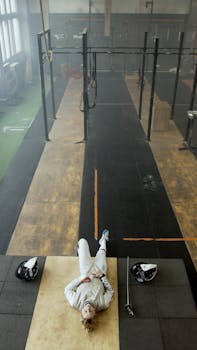 A woman in fencing attire resting on the gym floor viewed from above.