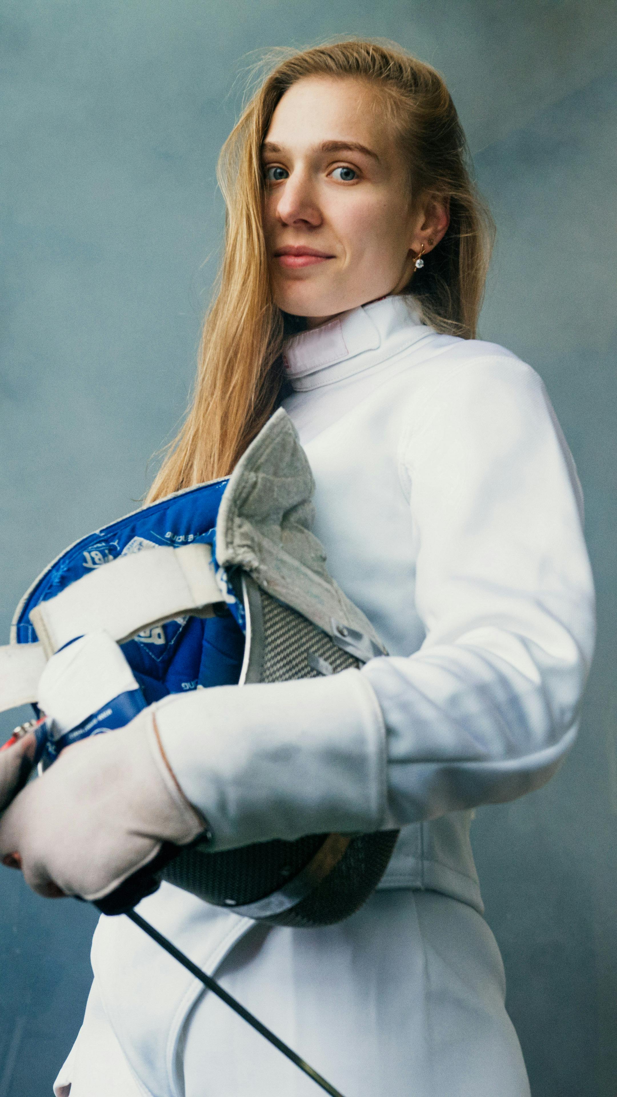 Portrait of a female fencer confidently holding her mask, exemplifying strength and focus.