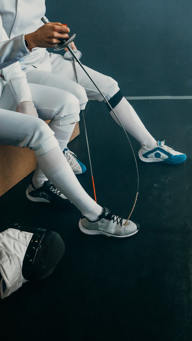 Two Young People Wearing White Fencing Uniforms Holding Swords