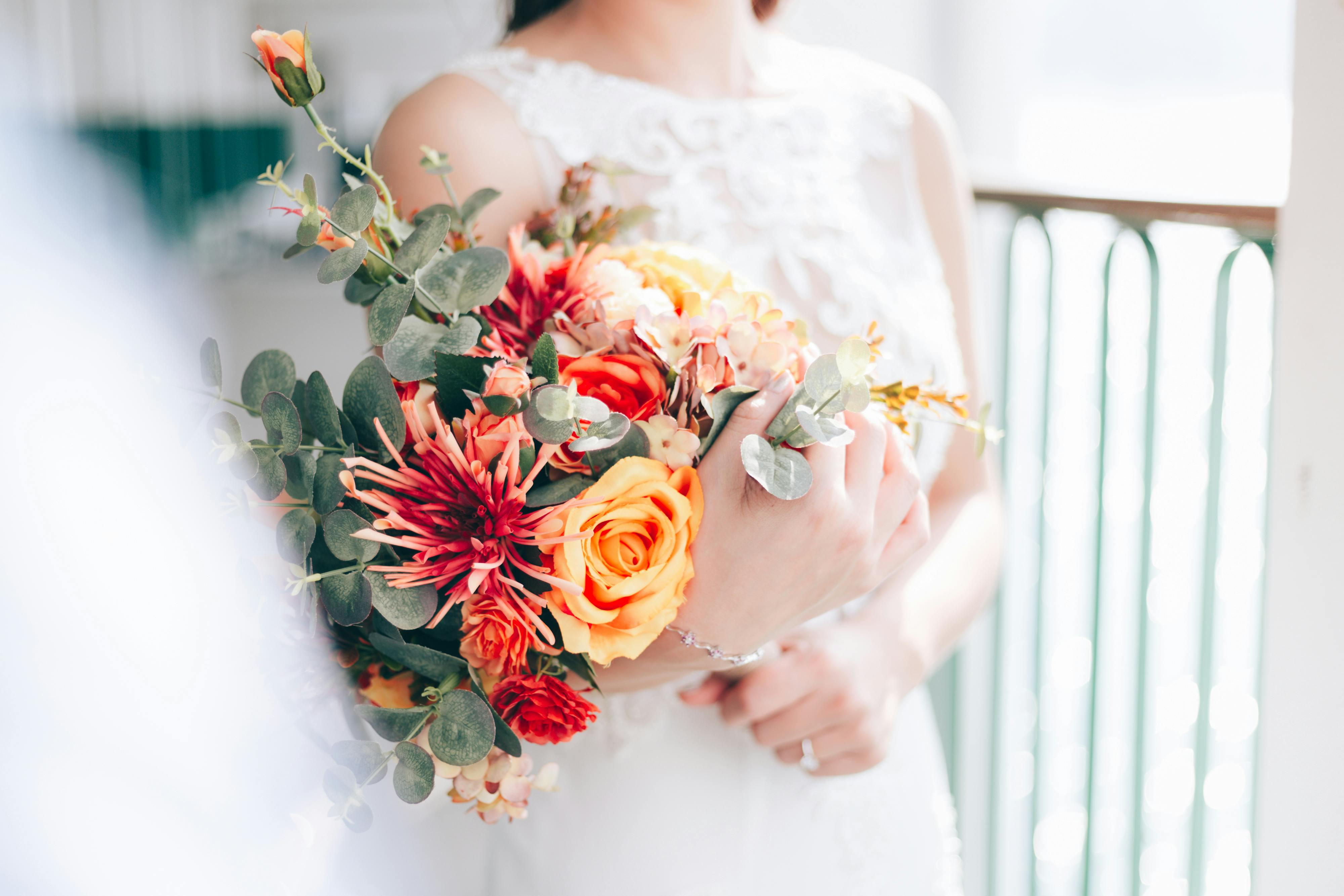 A bride holding a bright and colorful bouquet featuring roses and eucalyptus.
