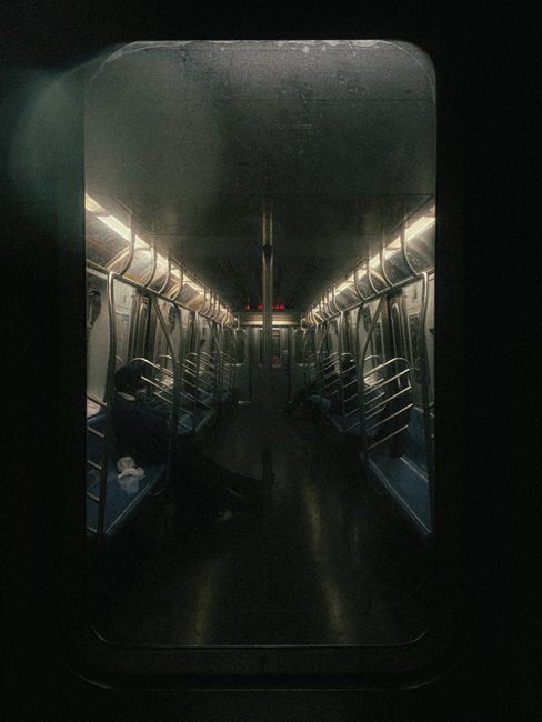 Through glass view full body side view of faceless people sitting on seats in train wagon with metal handrails in subway