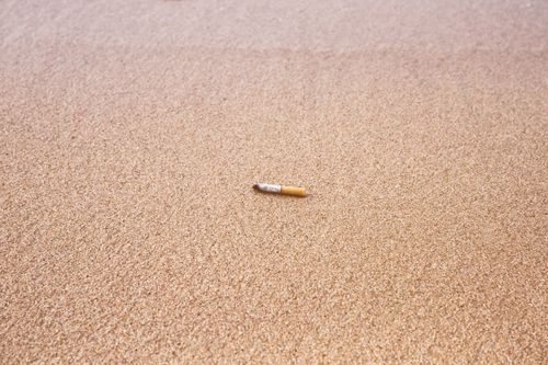 Free Cigarette butt discarded on a sandy beach, highlighting pollution. Stock Photo