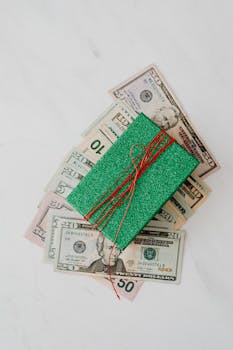 A green glitter gift box placed on US dollar bills, symbolizing wealth and finance.