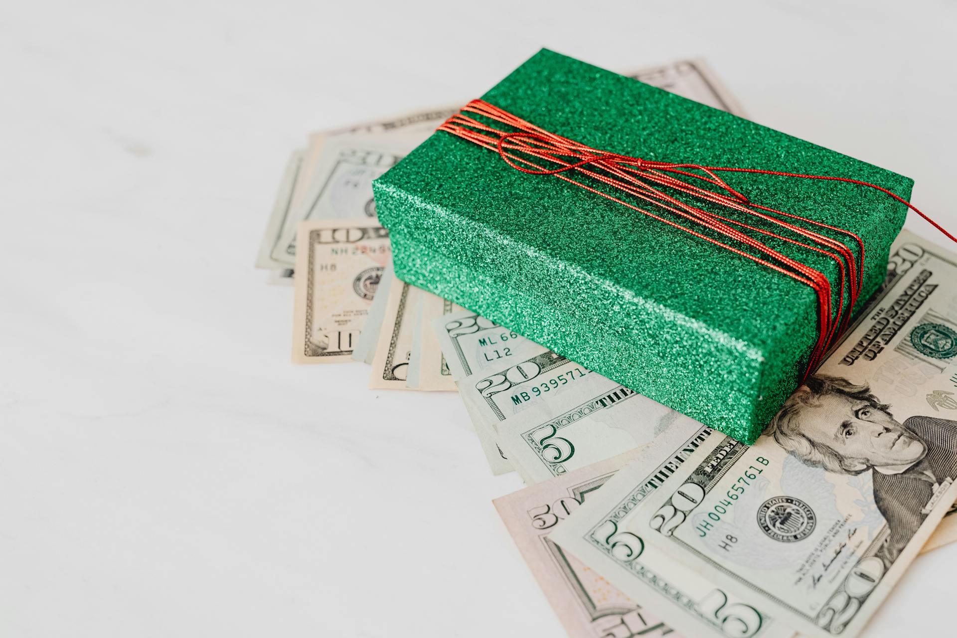 A sparkling green gift box sits atop scattered US dollar bills, emphasizing wealth and generosity.