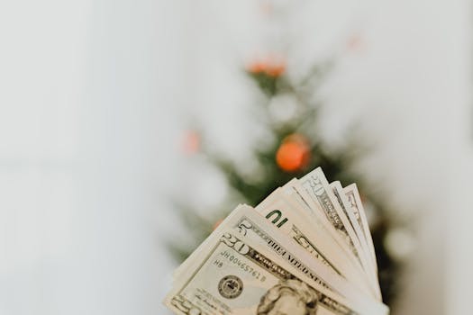 A close-up shot of US dollar banknotes with a blurred tree in the background, suggesting festive savings.