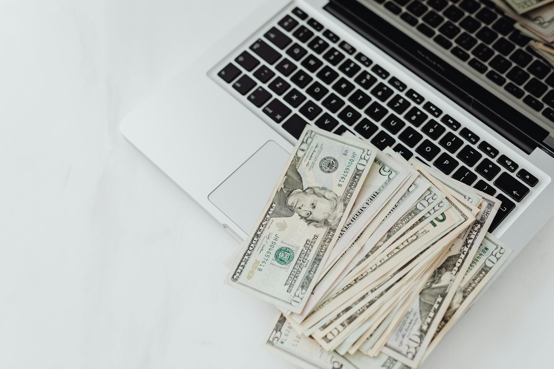 A stack of US dollar bills on a laptop keyboard representing online finance and budgeting.