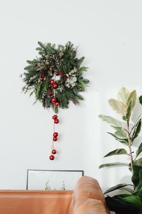 Free Elegant Christmas wreath with red ornaments on white wall in a stylish living room, enhancing holiday decor. Stock Photo